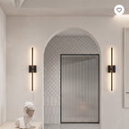 A modern bathroom interior with two slim black wall sconces mounted on cream walls on either side of an arched doorway. The sconces have vertical light bars that glow warm white.