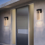 Two modern outdoor wall sconces with textured clear glass and black metal frames, mounted on a concrete building facade flanking a glass door.