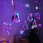 Multicolor LED hanging Christmas string lights shaped like stars, bells, bows, and a reindeer, displayed on a wall above a decorated Christmas tree.