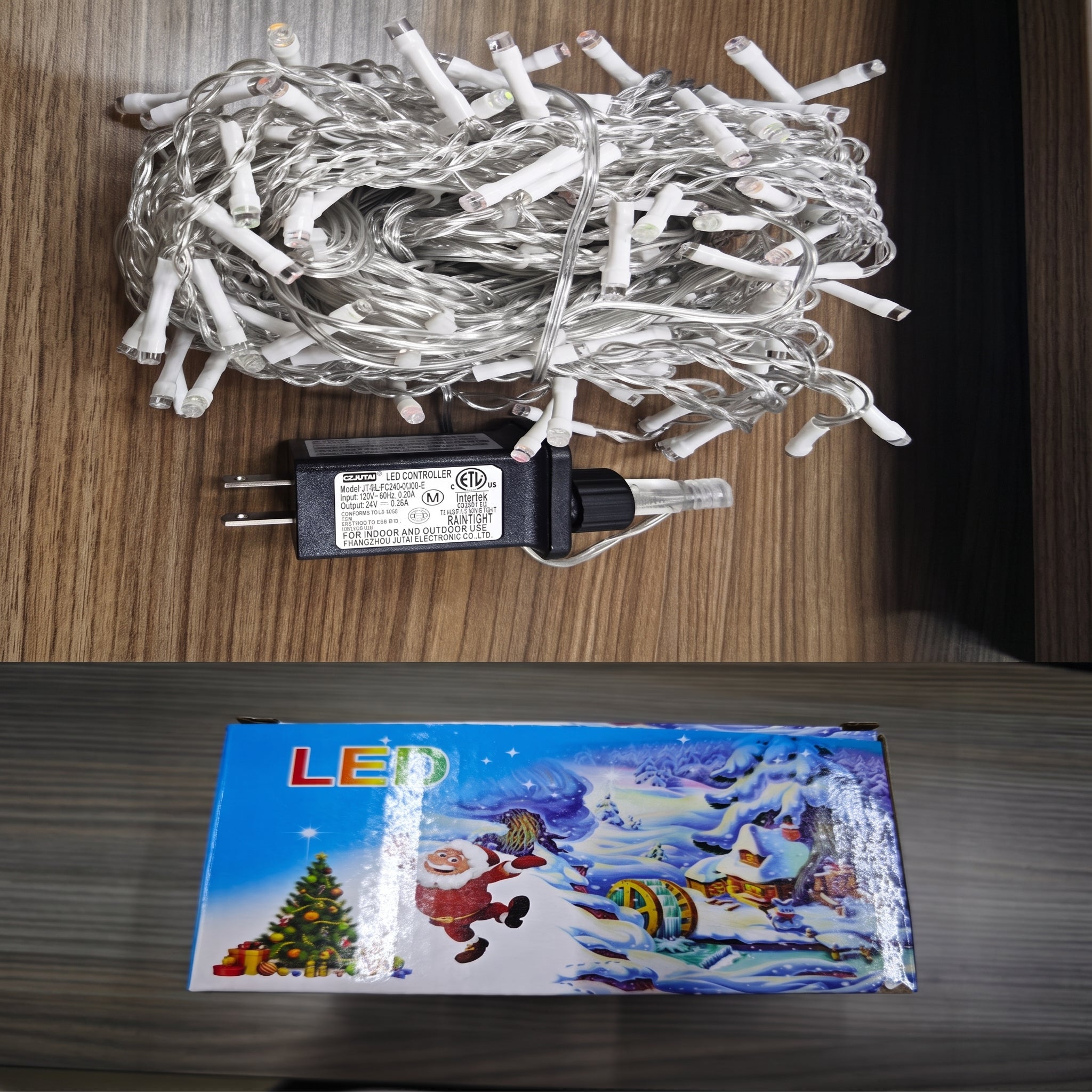 A coiled roll of white LED Christmas string lights with a black power adapter placed on a wooden surface, with the product box below showing a colorful winter holiday scene.