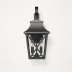 A black outdoor wall sconce with a lantern-style frame and two visible bulbs, mounted against a light textured wall.