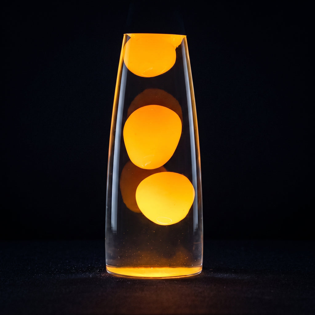 A clear glass lava lamp-style vase with three glowing orange-yellow blobs floating in transparent liquid, photographed against a black background.