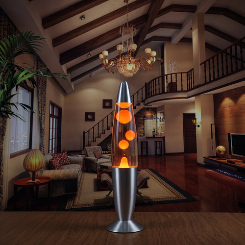 A modern lava lamp with a silver metal base and clear glass cone, featuring glowing orange bubbles, set on a wooden table in a warmly lit, high-ceilinged living room.