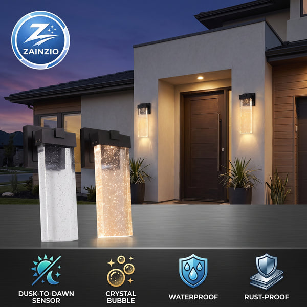 Two Zainzio outdoor LED light posts shown in front of a modern house at dusk, with one post turned off and one turned on to show the illuminated crystal bubble effect. The image includes feature icons at the bottom for dusk-to-dawn sensing, crystal bubble, waterproof, and rust-proof.