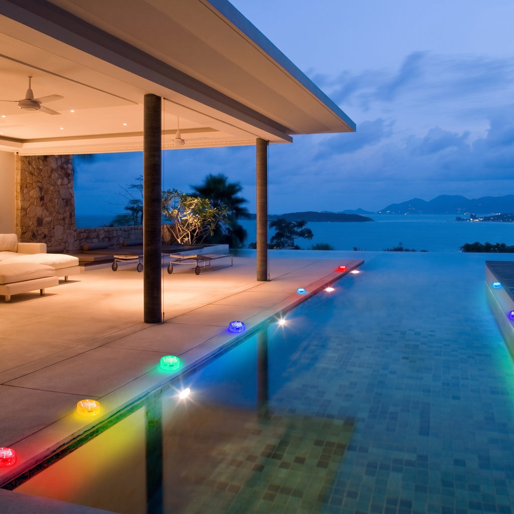Outdoor pool area with colorful lights at dusk, overlooking a scenic view.