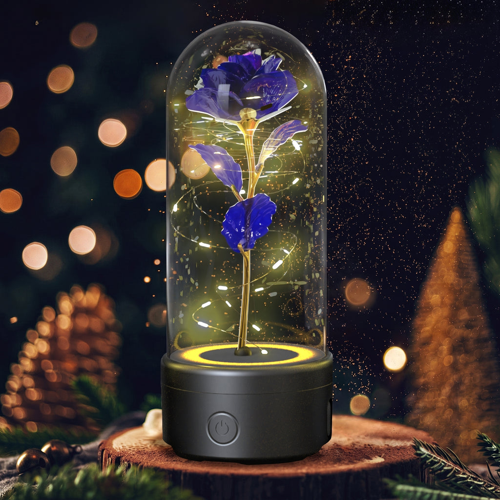 A preserved blue rose under a clear glass dome on a black base with warm yellow fairy lights, displayed on a wooden surface with festive blurred lights and pinecones in the background.