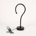 A modern black metal table lamp with a curved hook-shaped arm and a round base, shown with its power cord on a clean white background.