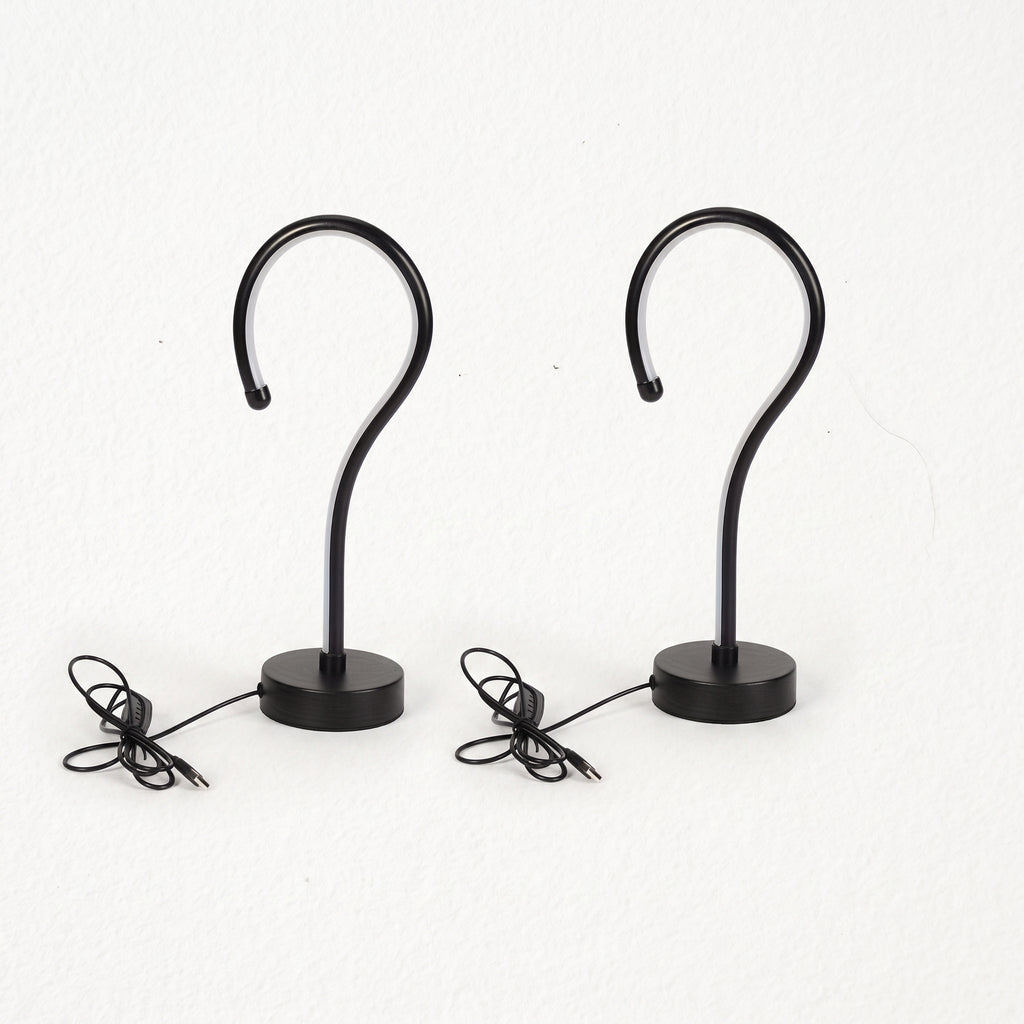 Two black metal S-shaped wall hooks with round bases and attached power cords, shown against a plain white background.