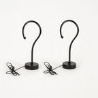 Two black metal S-shaped wall hooks with round bases and attached power cords, shown against a plain white background.