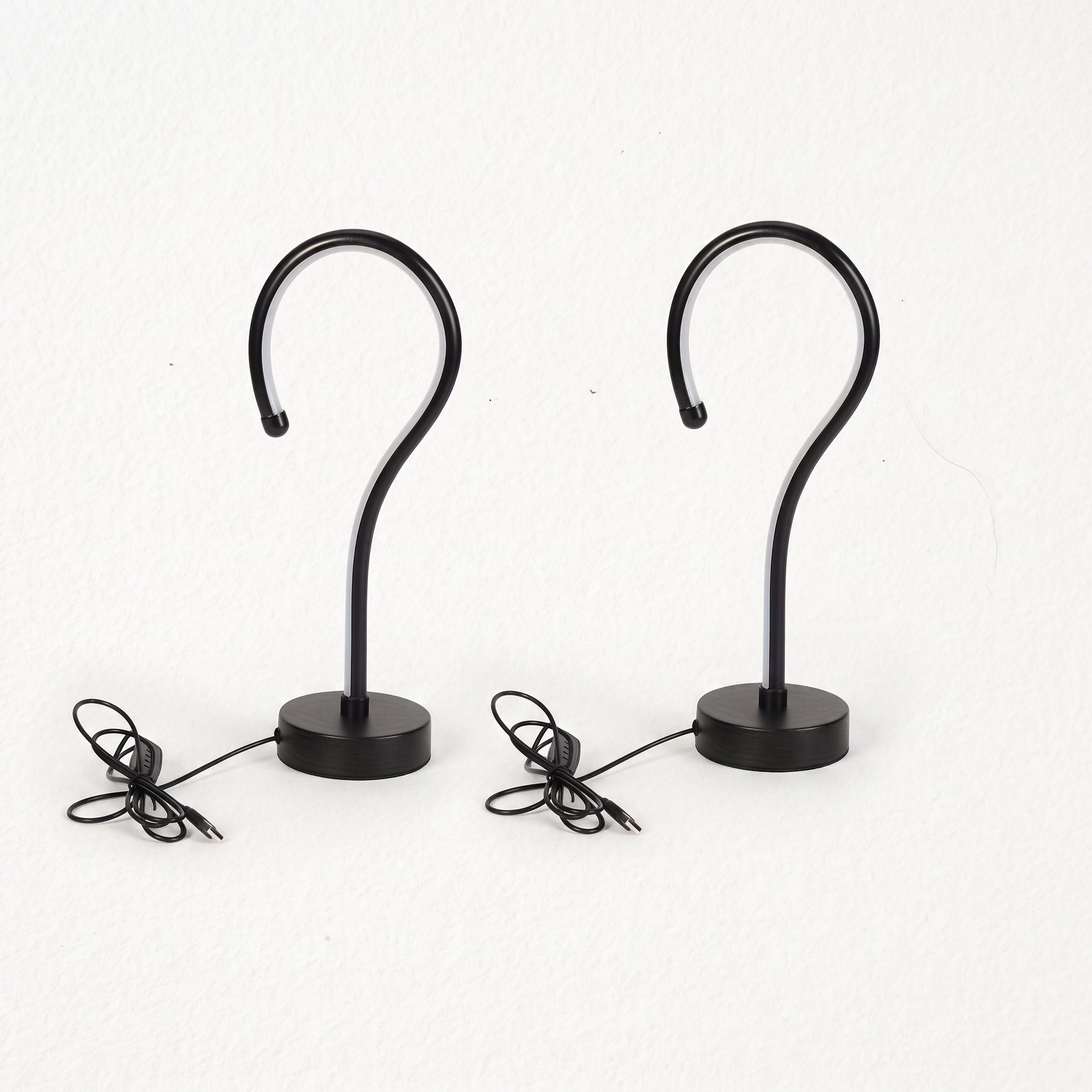 Two black metal S-shaped wall hooks with round bases and attached power cords, shown against a plain white background.