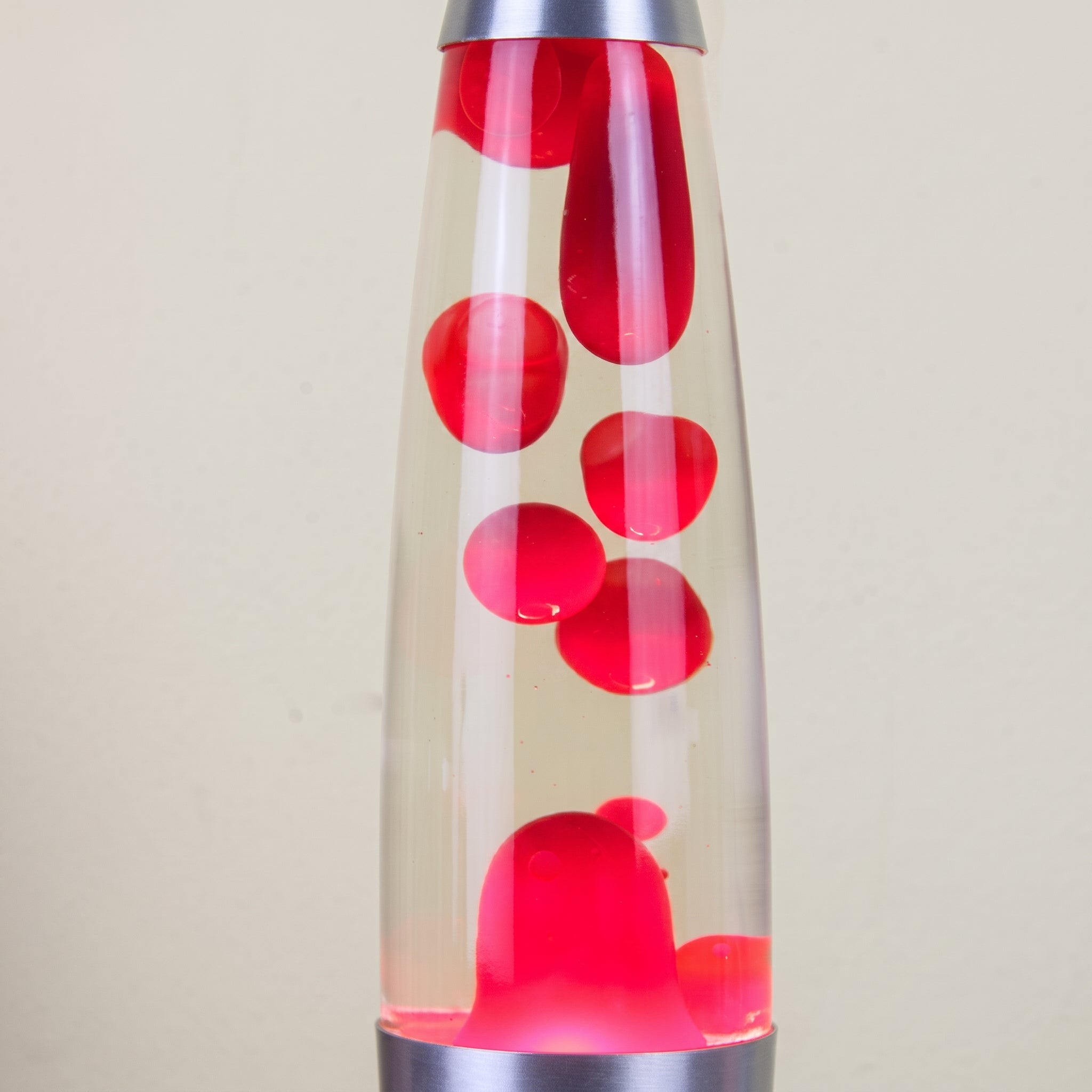 A classic lava lamp with a clear glass body, filled with bright red wax blobs and a silver metal base and top cap, set against a plain beige background.