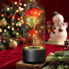 A glowing LED light-up rose under a clear glass dome on a black base, set on a wooden block with a blurred Christmas tree and snowman in the background.