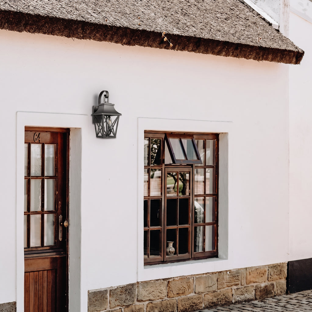 A white stucco building facade with a thatched roof edge, a dark wall lantern, a wooden door with glass panes, and a matching wooden multi-pane window set over a stone base.