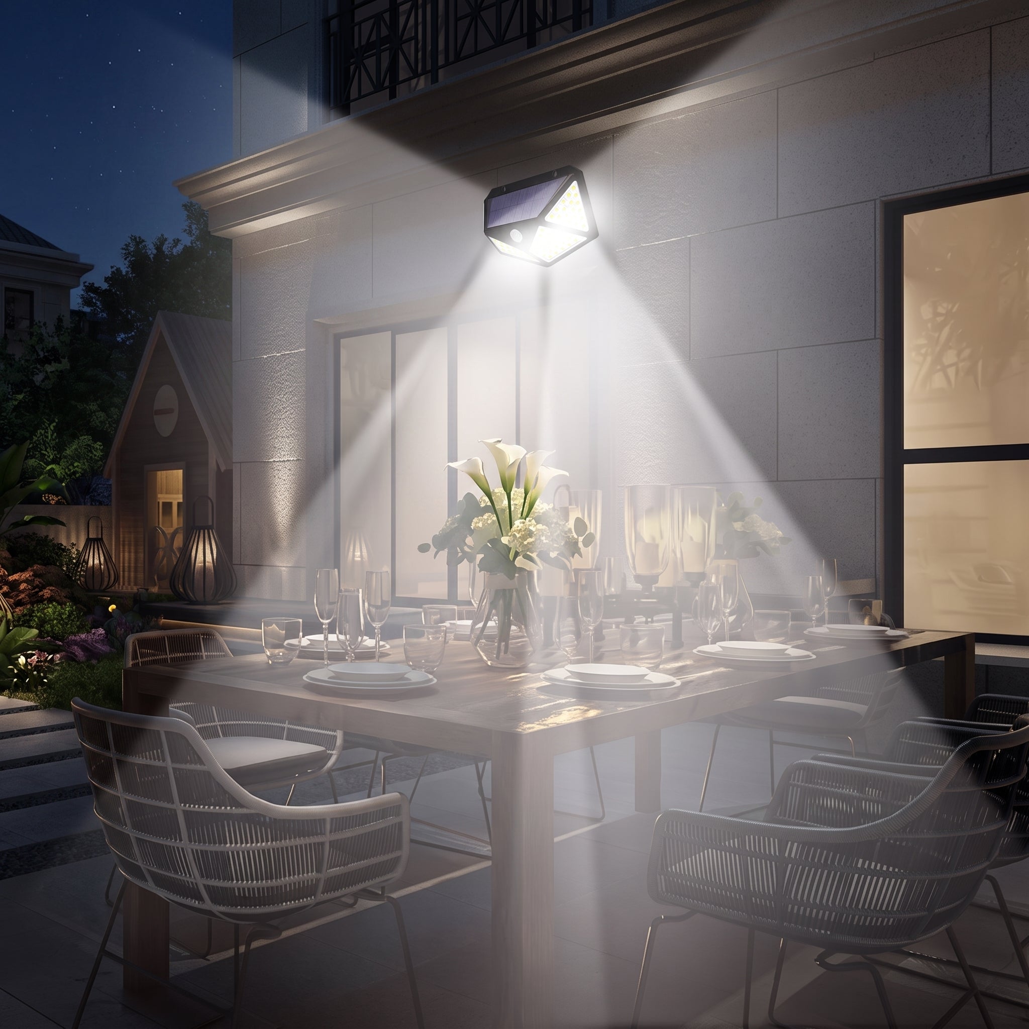 Outdoor wall sconce lighting a dining table at night, casting a bright beam of light across a set dining set on a patio beside a modern house.