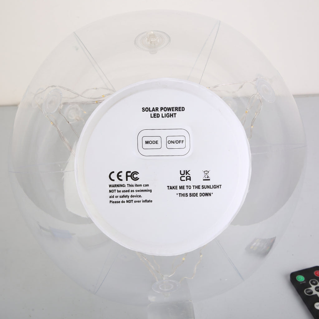Top-down view of a solar-powered LED light on an inflatable ring, showing the white circular control panel with mode and on/off buttons, CE and UKCA certification marks, and a small remote control in the corner.