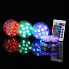 Four round LED light pods in red, green, blue, and purple, shown with a white remote control on a black reflective background.