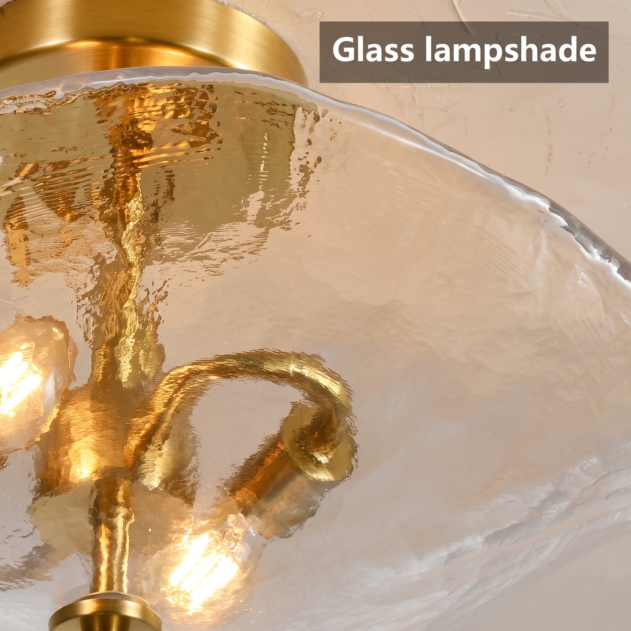 Close-up of a gold metal ceiling light fixture with a textured, wavy clear glass shade, showing illuminated bulbs inside. A text overlay in the top right reads 'Glass lampshade'.