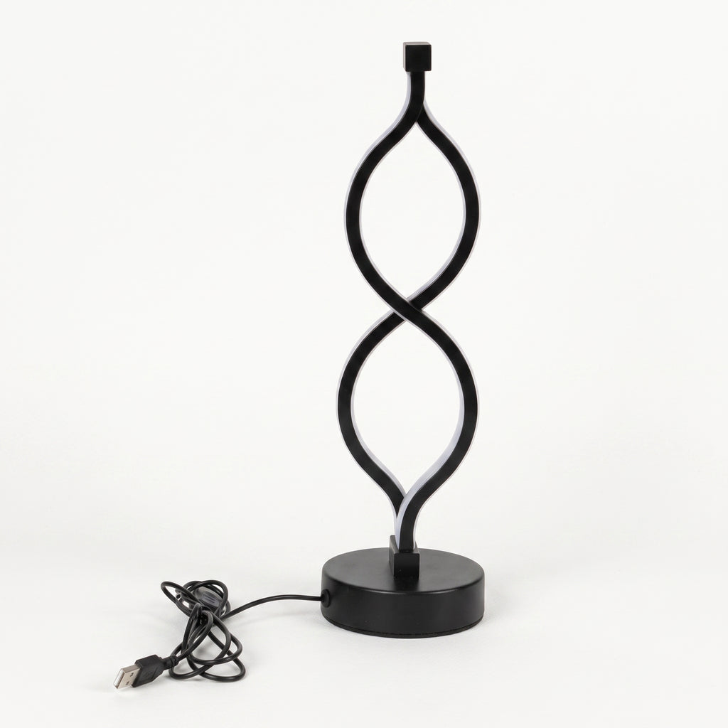 A modern black LED table lamp with a sculptural, twisting infinity-loop design on a round base, shown with its USB charging cable on a white background.