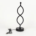 A modern black LED table lamp with a sculptural, twisting infinity-loop design on a round base, shown with its USB charging cable on a white background.