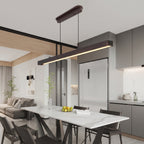 A modern linear LED pendant light with a dark brown wood-look frame hangs over a dining table in a contemporary kitchen and dining room setting.